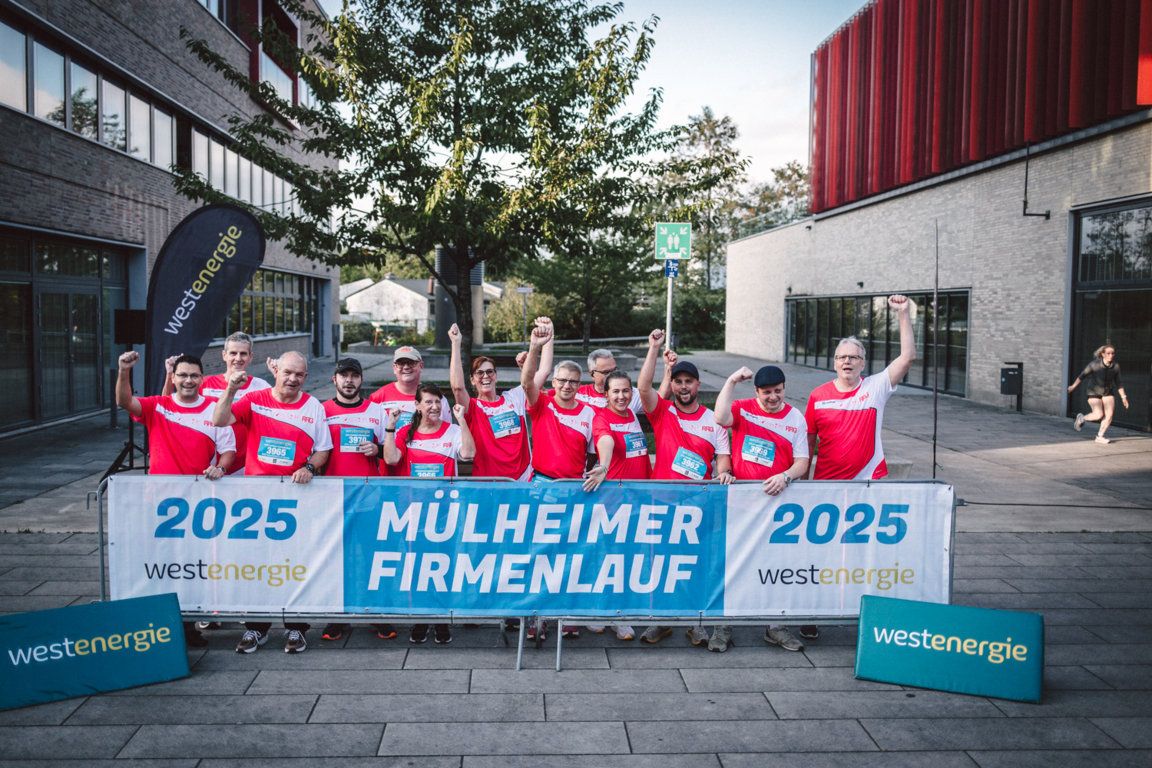 RRG-Team in roten Lauftrikots beim 9. Mülheimer Firmenlauf 2025, Gruppenfoto mit erhobenen Fäusten vor dem Westenergie-Banner