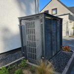 Seitenansicht links: Premium Sichtschutzgehäuse für eine Wärmepumpe – robuste Stahlverkleidung in Anthrazit (RAL 9017) mit Schrägdach, Lochblechseiten für Belüftung und offener Rückseite für Zuleitungen.